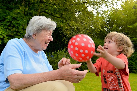 Kind und Seniorin spielen mit einem roten Ball