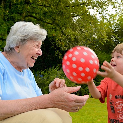 Kind und Seniorin spielen mit einem roten Ball