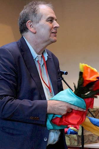 Ludger Hoffkamp ist Clown und Seelsorger, hier bei einem Vortrag in der Stiftung Großheppacher Schwesternschaft. Er hält einen Strauß aus Papierblumen in der Hand.