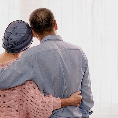 Ein Paar, das sich umarmt, steht mit dem Rücken zum Betrachter und schaut auf eine weiße Fläche.