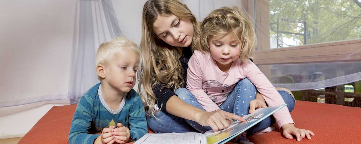 Eine junge Frau liest einem kleinen Jungen und einem kleinen Mädchen aus einem Bilderbuch vor